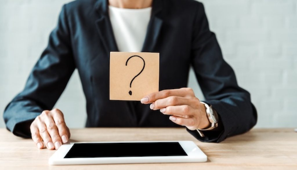 cropped view of woman holding sticky note with question mark near digital tablet