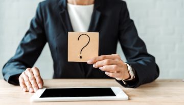 cropped view of woman holding sticky note with question mark near digital tablet