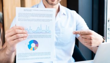 cropped view of smiling man pointing with finger at document with diagram in cafe