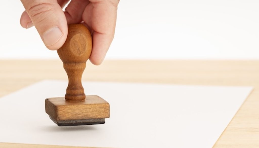 Hand holding a Rubber stamp and blank paper on wooden table. Copy space