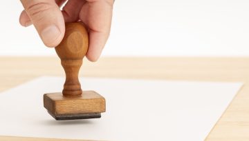 Hand holding a Rubber stamp and blank paper on wooden table. Copy space