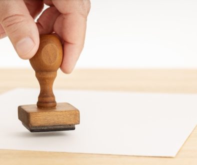 Hand holding a Rubber stamp and blank paper on wooden table. Copy space